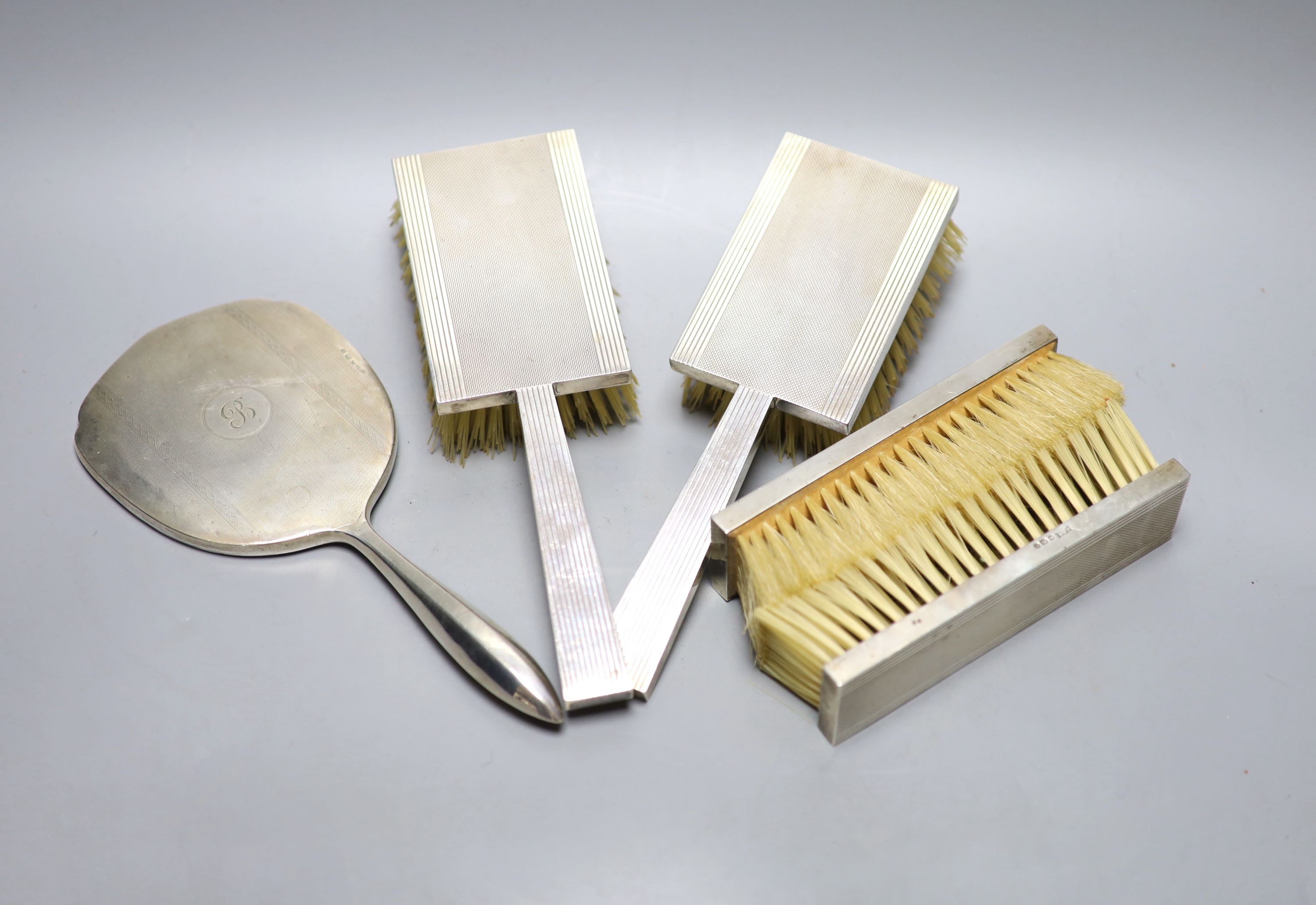 A 1930's engine turned silver backed four piece dressing table set, Birmingham, 1936 and a silver mounted hand mirror.